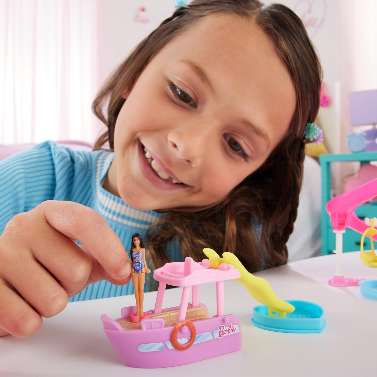 Mini BarbieLand doll and toy vehicle set featuring a 1.5-inch Barbie doll, colorful dream boat, slide, and pool with color-change features.