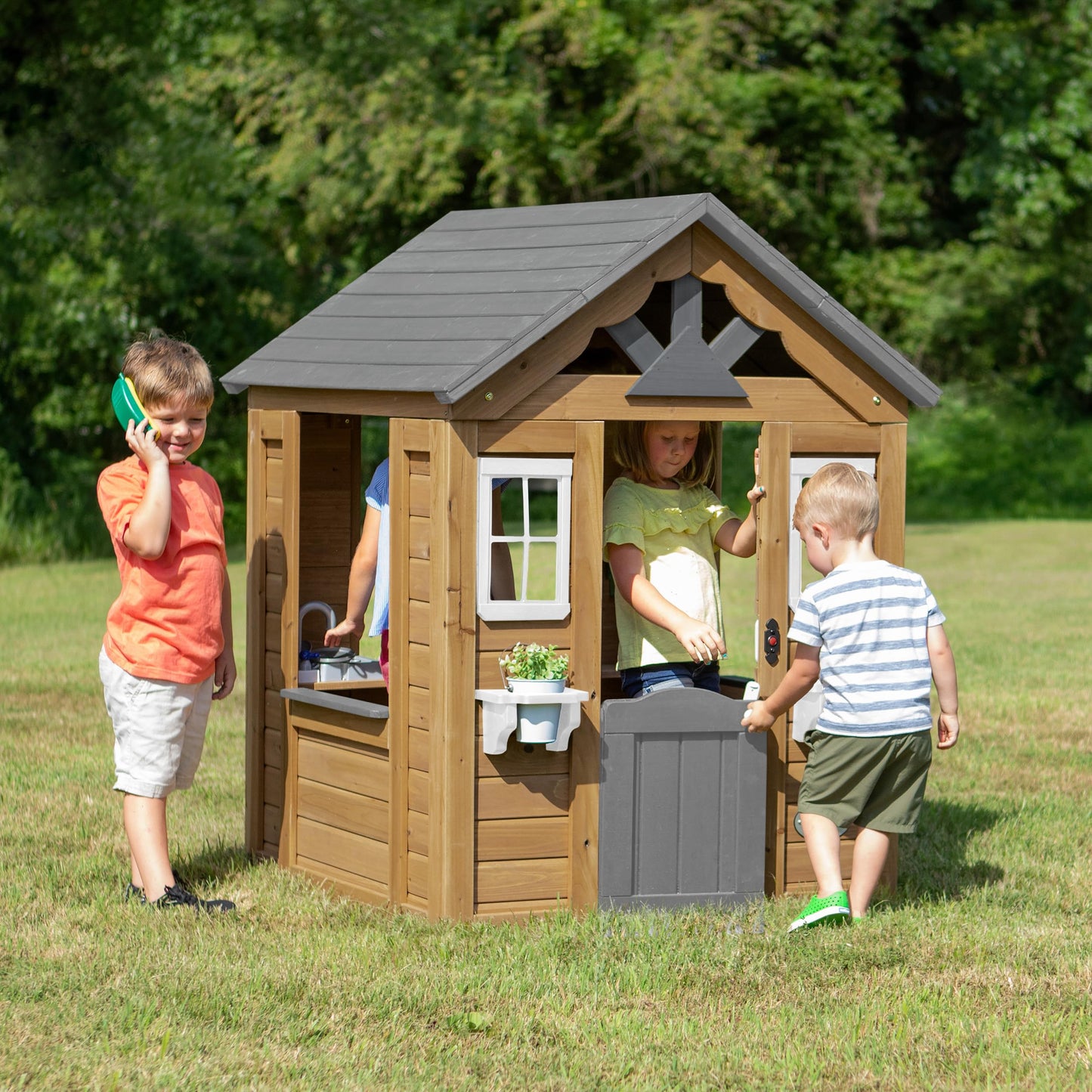Backyard Discovery cedar wood children's playhouse with play kitchen, snack bar window, and half door in a backyard garden setting.