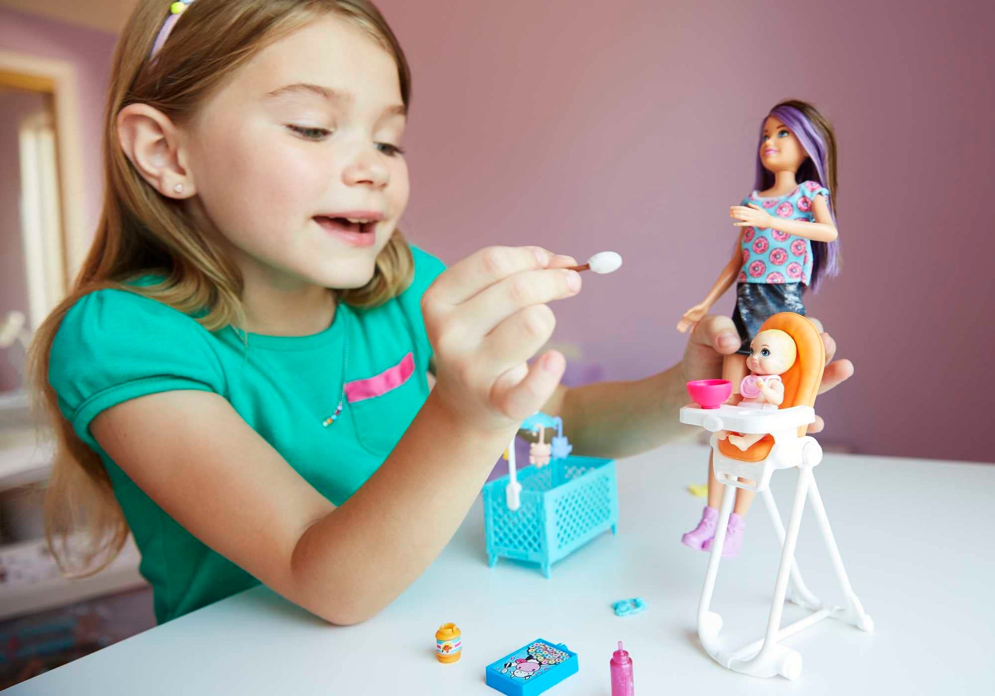 Barbie FHY98 Family Babysitter Brunette Doll with baby and highchair playset in a colorful scene, showcasing accessories.