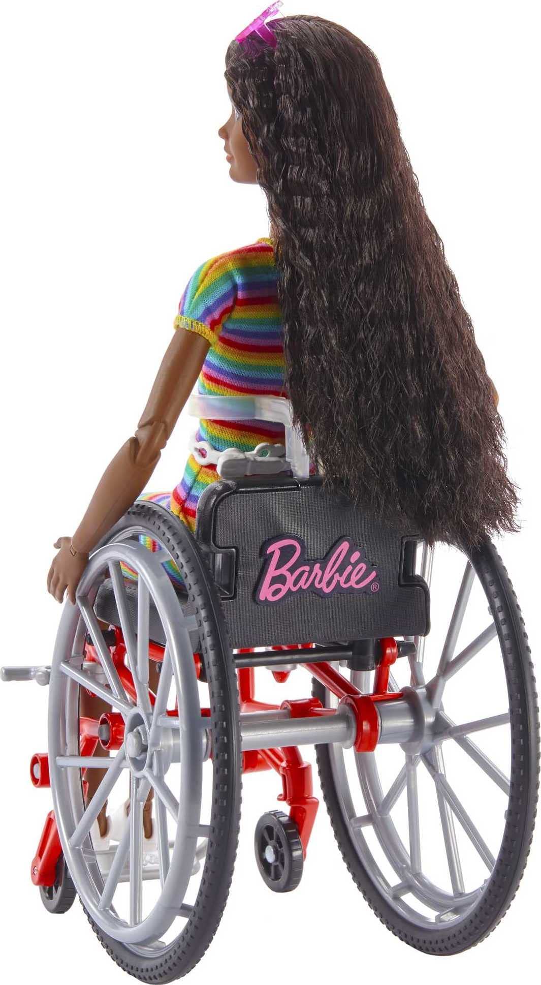 Barbie Fashionistas Doll #166 with wheelchair, crimped brunette hair, rainbow dress, white sneakers, sunglasses, and fanny pack.