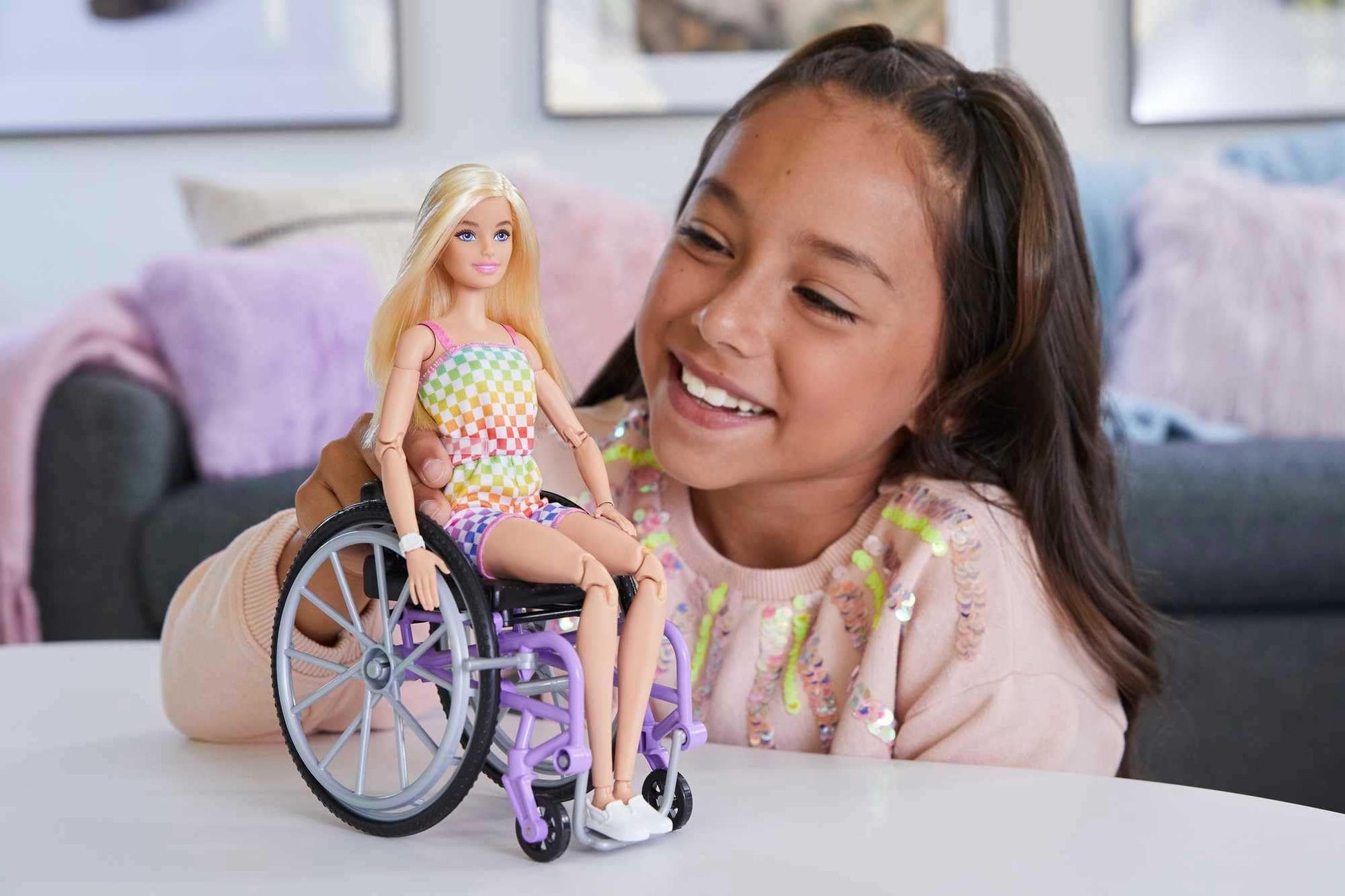 Barbie Fashionistas doll in a rainbow romper, seated in a wheelchair with a ramp, featuring blonde hair and accessories.