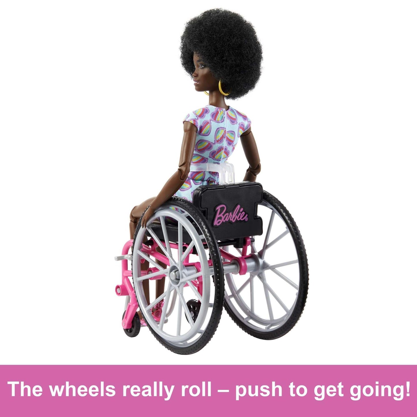 Barbie Fashionistas doll with curly black hair in a rainbow heart romper, sitting in a wheelchair with a ramp.