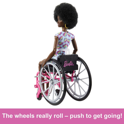 Barbie Fashionistas doll with curly black hair in a rainbow heart romper, sitting in a wheelchair with a ramp.
