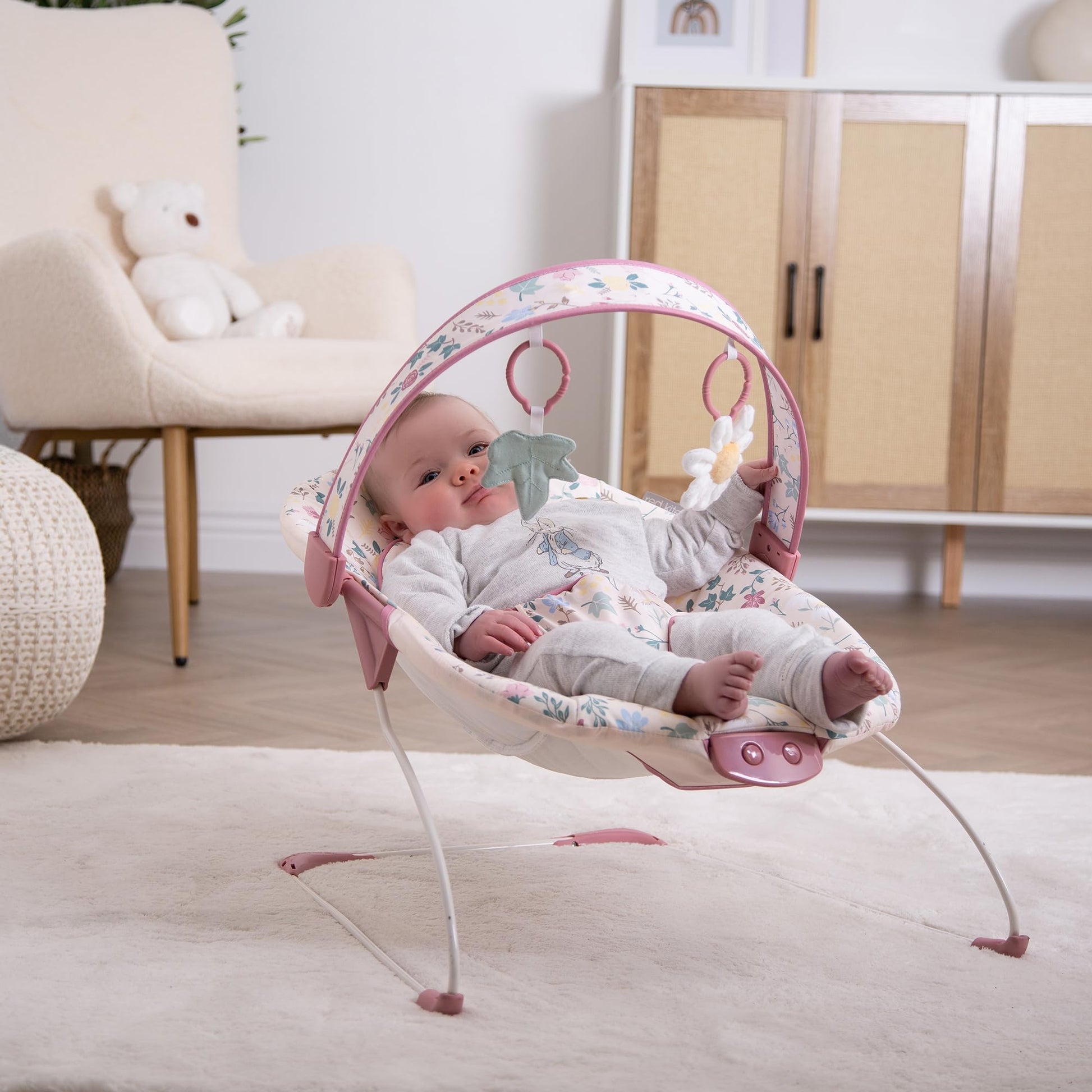 Red Kite Cozy Bounce musical baby bouncer in rose and ivy fabric with plush padding and a detachable toy bar for infants.