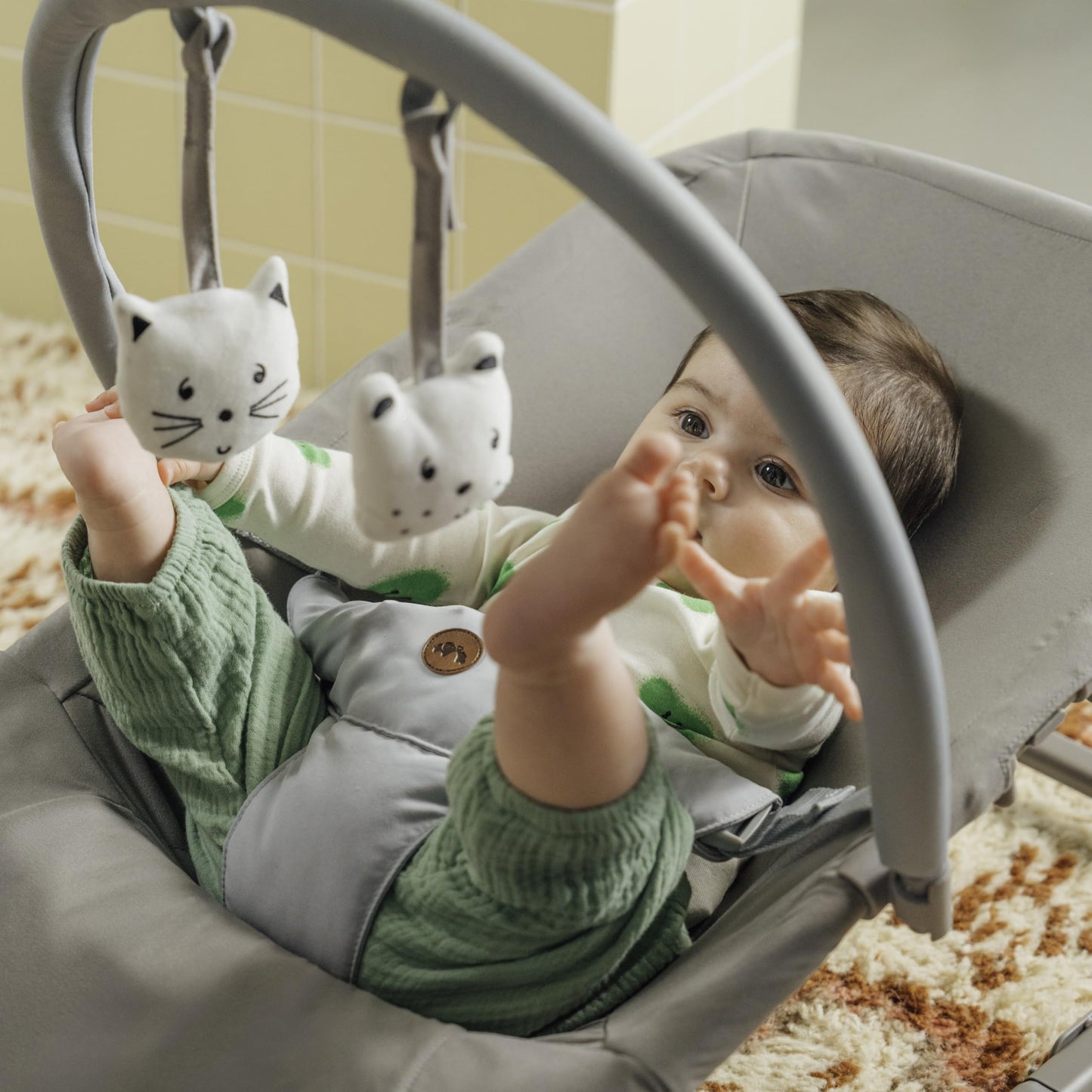 Bebeconfort Aster baby rocker in tinted graphite with adjustable backrest, removable toy arch, 3-point harness, in stationary mode.