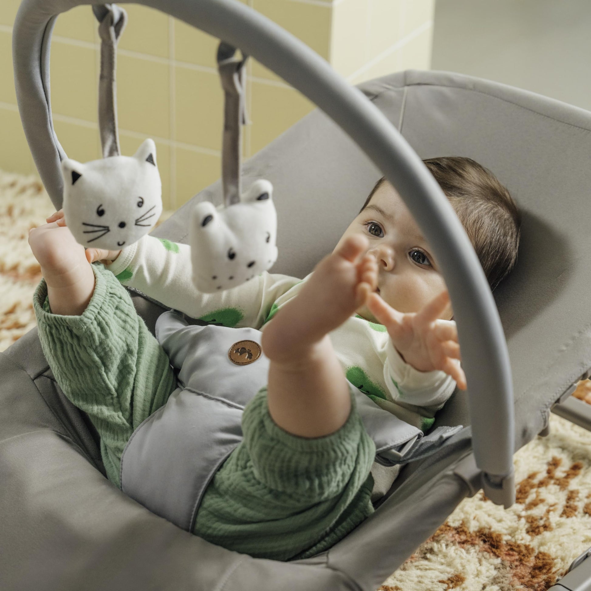 Bebeconfort Aster baby rocker in tinted graphite with adjustable backrest, removable toy arch, 3-point harness, in stationary mode.