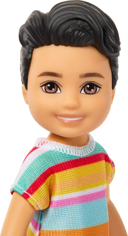 Barbie Club Chelsea Koji 6-inch boy doll with brunette hair, striped shirt, shorts, and shoes, posed outdoors.