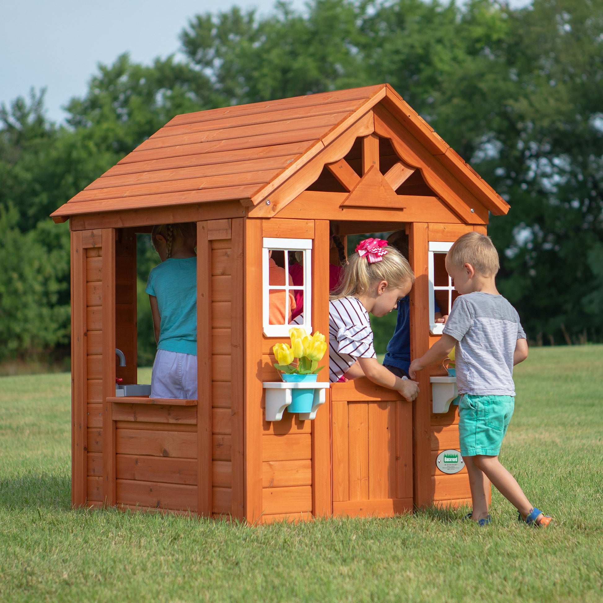 Backyard Discovery Timberlake cedar wood playhouse with toy kitchen, phone, and flowerpot holders, suitable for children aged 2-7.