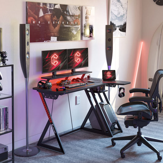 CubiCubi black L-shaped gaming desk with LED lights, monitor stand, shelves, hooks, and power outlets for home office and gaming.