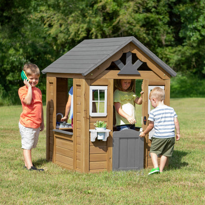 Backyard Discovery cedar wood children's playhouse with play kitchen, snack bar window, and half door in a backyard garden setting.