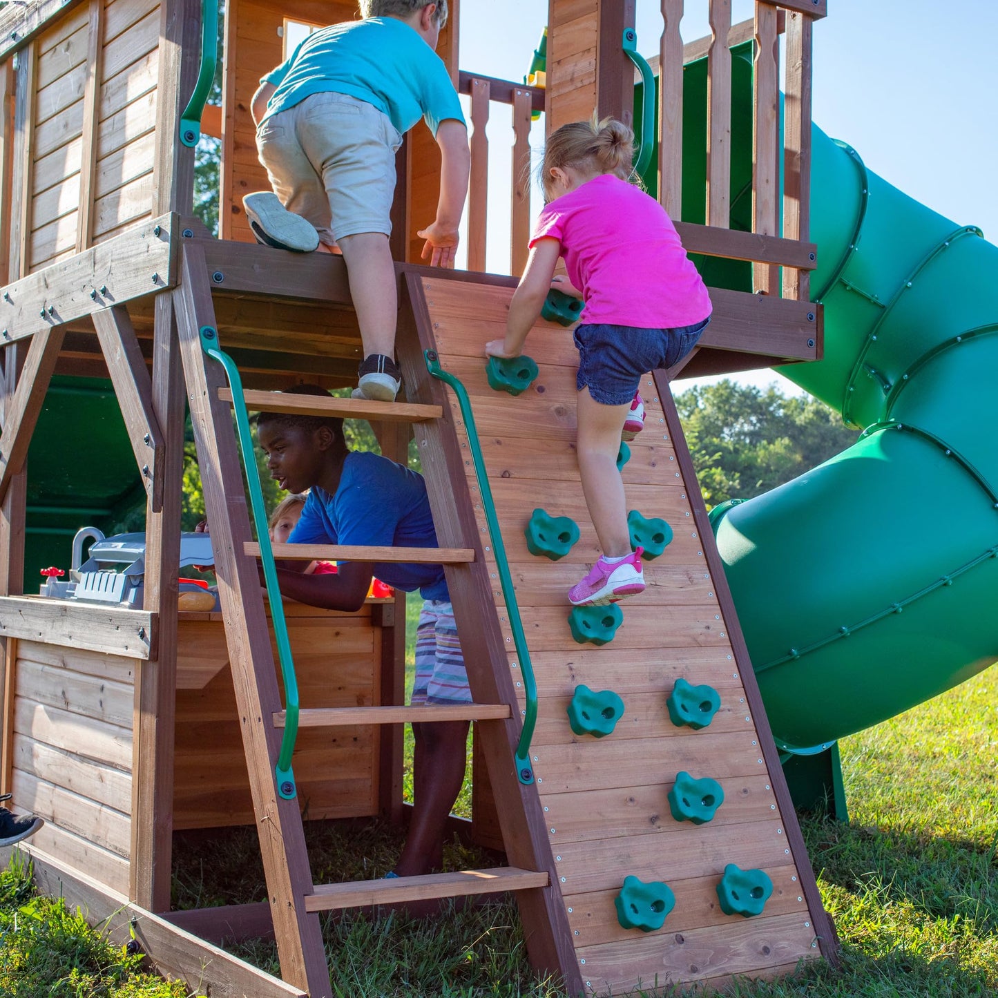 Backyard Discovery Cedar Cove cedar wood swing set with wave slide, tube slide, rock wall, web disc, and two belt swings in a backyard.